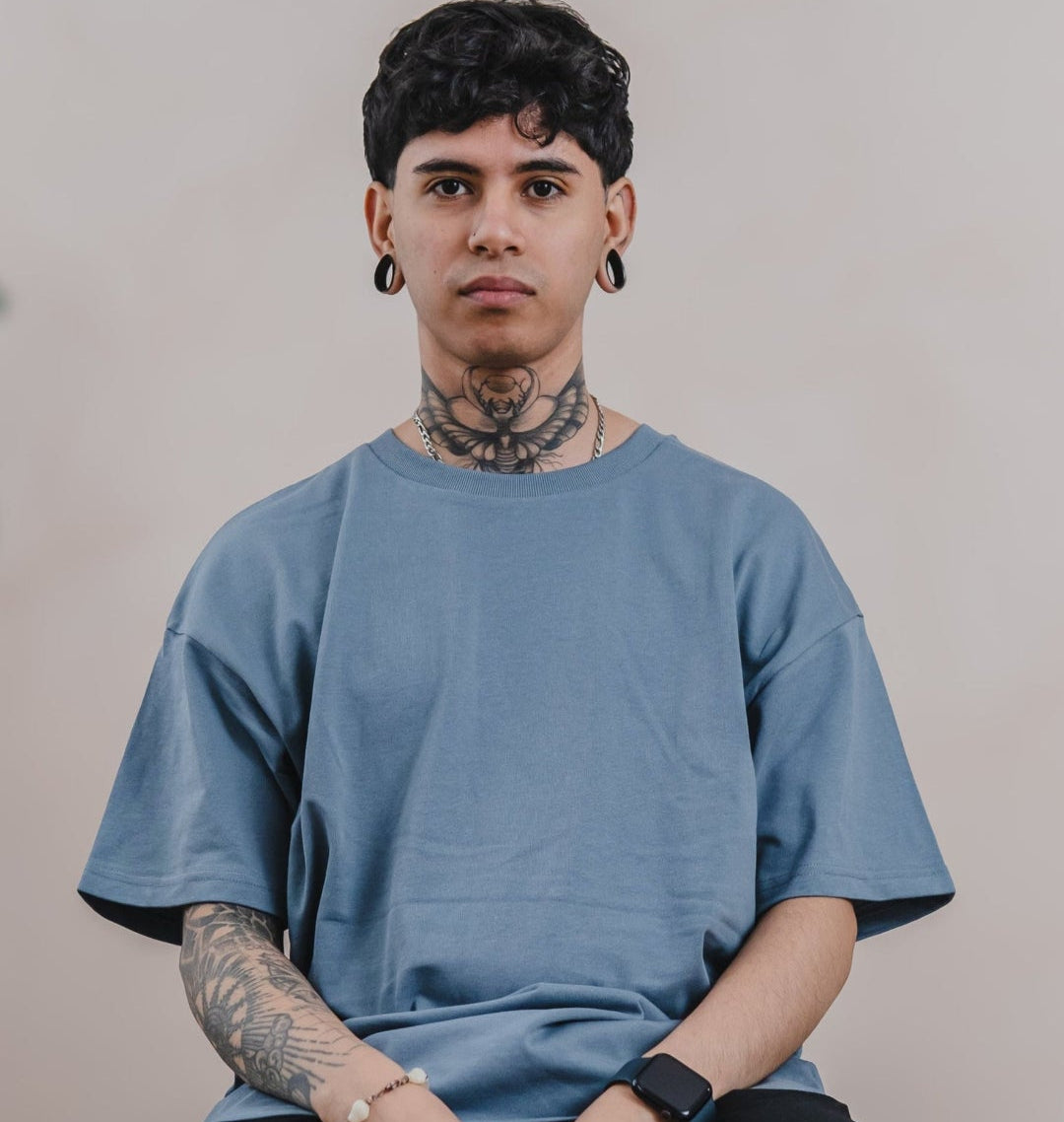 A Tattooed Man Sitting On A Chair, Wearing A Men's Oversized Organic T-shirt