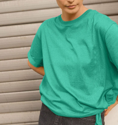 A woman in a green ReSprout relaxed fit t-shirt and jeans stands confidently, showcasing a casual and stylish look.