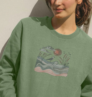 A woman in a green sweatshirt featuring a bird drawing, showcasing the sun and birds women's boxy fit organic jumper.