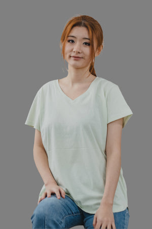 A woman in a green V-neck organic T-shirt and jeans stands confidently, showcasing a casual and eco-friendly style.