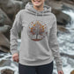 A woman in a grey hoodie featuring an autumn tree design, showcasing the Inner Peace Women's Pullover Organic Hoodie.