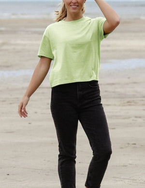 A Woman In a Lime Green Boxy Fit Organic T-shirt Walks Along The Beach
