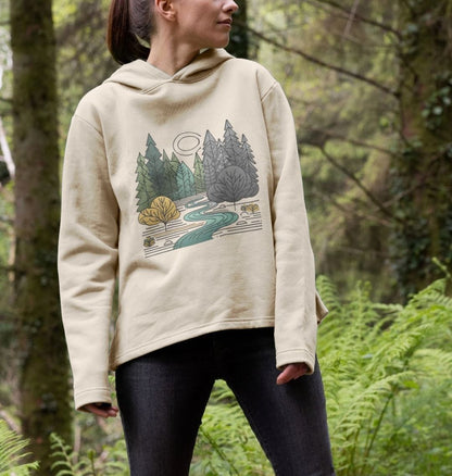 A woman in a relaxed fit hoodie featuring a serene forest scene