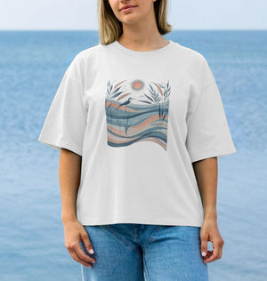 A woman in a white oversized t-shirt featuring a bird and waves design, showcasing a casual and artistic style.
