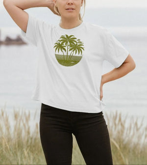 A woman in a white t-shirt featuring palm trees, showcasing a tropical sunset design in a boxy fit style