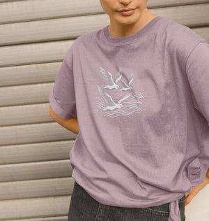A woman models a purple organic T-shirt with a seagull design, part of the Waves and Wings collection