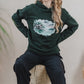 A woman wearing a green Woodhouse hoodie with a ship design, highlighting a relaxed fit and casual style.