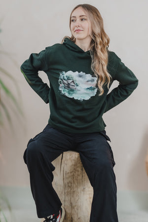 A woman wearing a green Woodhouse hoodie with a ship design, highlighting a relaxed fit and casual style.